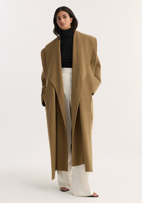 Woman models the Signature double-faced scarf coat in camel, showcasing its double-layered scarf collar, tailored silhouette, and double-breasted design over a minimalist outfit.