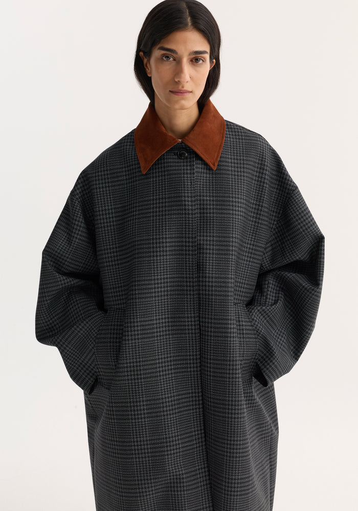 Model wears an oversized Suede collar check coat | black / grey check with a rust-brown suede collar, visible button, and hands in pockets.