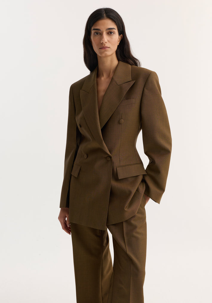 Model in a golden brown double-breasted waisted blazer with peak lapels, strong shoulders, and wide-leg trousers, showcasing a tailored, structured silhouette.