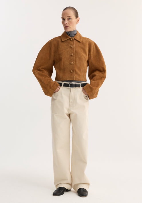 Person in a Rounded textured suede jacket | cognac, featuring a cropped, waisted fit and structured sleeves, paired with a turtleneck, trousers, and loafers.