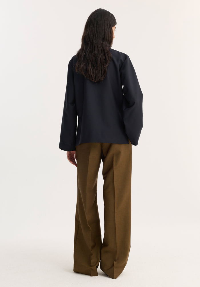 Person wearing a navy Mandarin jacket with a pankou closure and patch pockets, styled with wide-leg trousers, showcasing minimalist elegance.