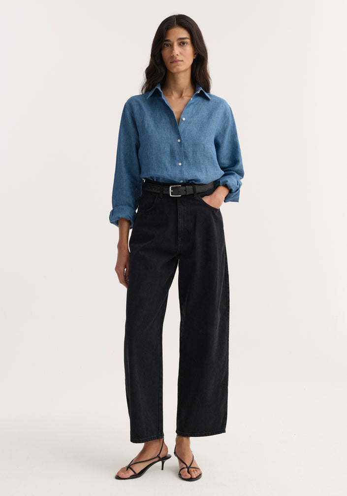 Woman wearing a Classic chambray shirt in ocean blue, styled with high-waisted black wide-leg jeans and black strappy heeled sandals.