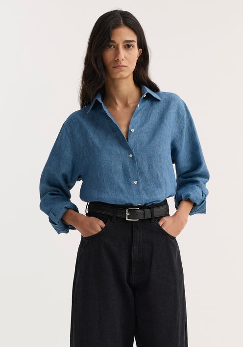 Woman wearing a Classic chambray shirt in ocean blue, styled with high-waisted black wide-leg jeans and black strappy heeled sandals.