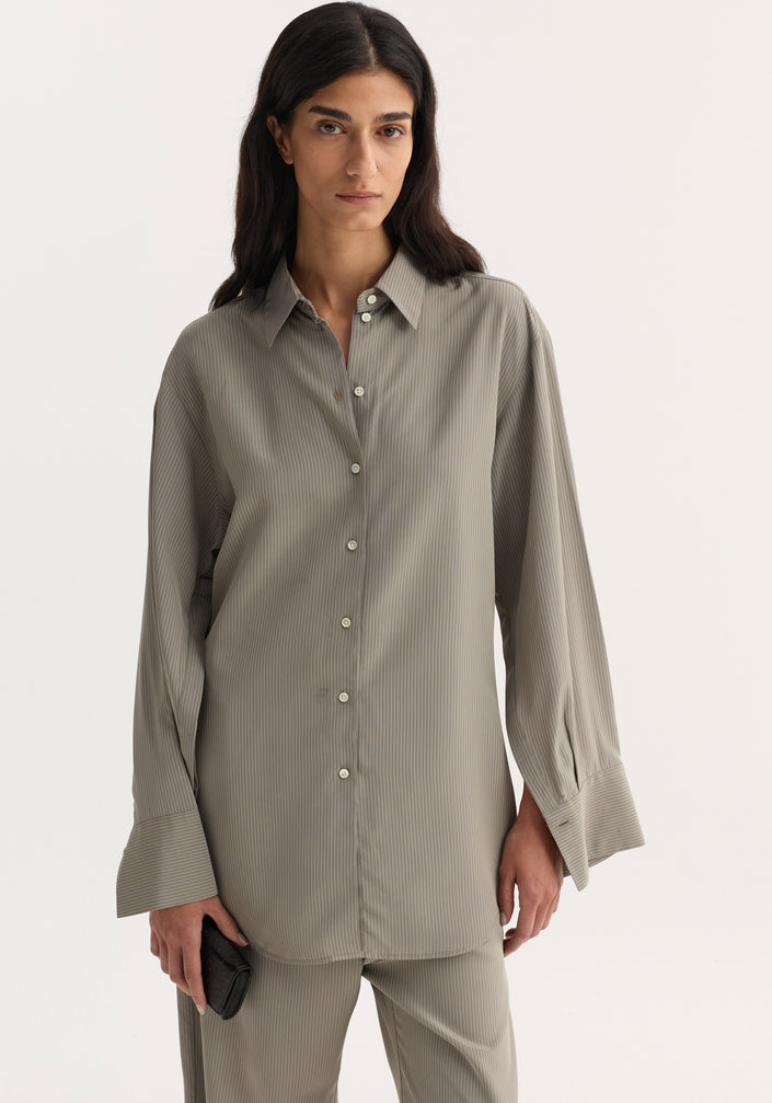 The woman models a Relaxed shaped shirt | light grey stripe, showcasing its loose fit, elongated sleeve plackets, and mother-of-pearl buttons, paired with matching trousers.