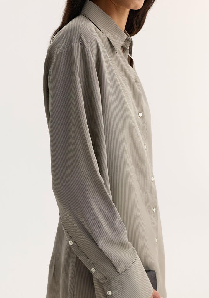 Side-view of a person wearing the Relaxed shaped shirt | light grey stripe, showcasing its button-down design, fine pin-stripes, and elongated sleeve plackets.