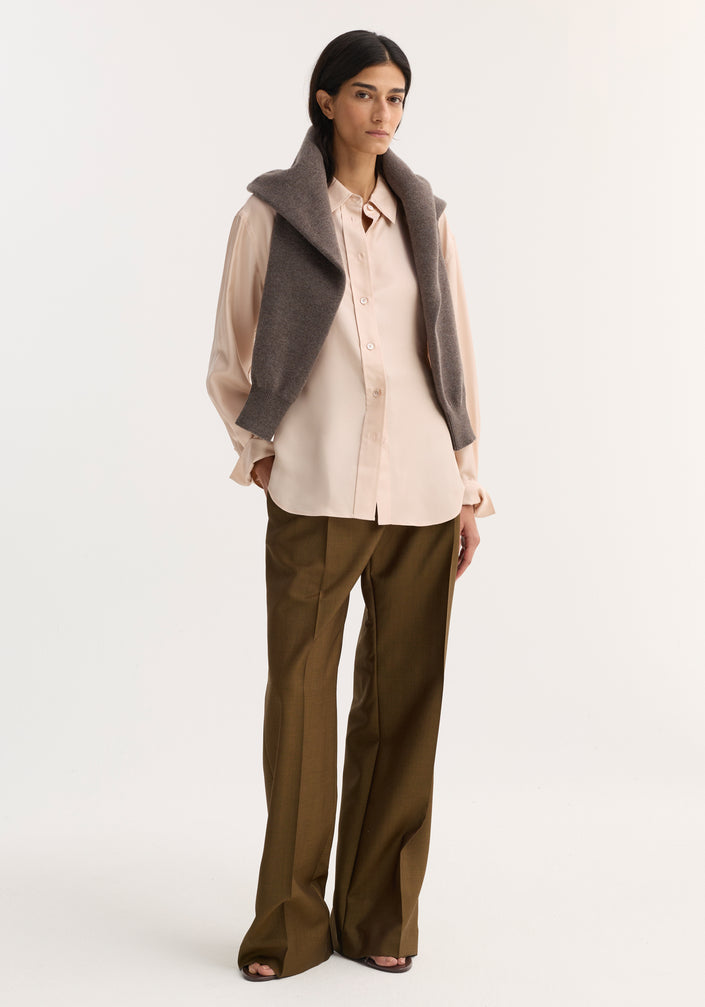 Silk shaped shirt in rose, featuring a relaxed hourglass silhouette with a button-down front and rounded hem, modeled with a knit sweater and wide-leg trousers.