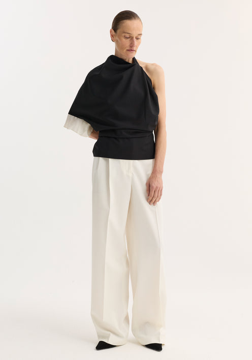 Model in a Draped open back wool top | black, featuring an asymmetric, single-sleeve design, paired with high-waisted, wide-leg trousers, showcasing minimalist, architectural style.