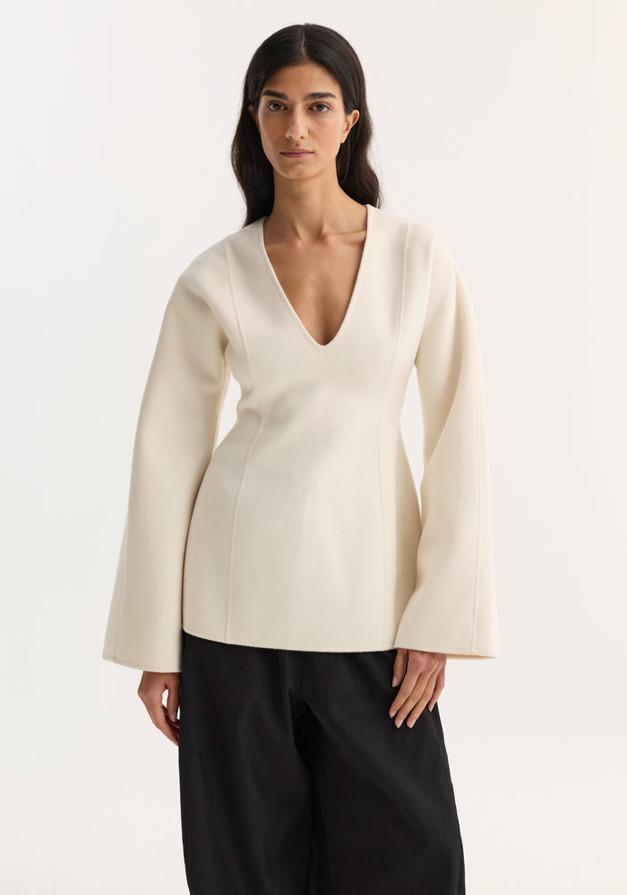 Model wearing Sculptural long sleeve top | off white with voluminous sleeves and a V-neckline, paired with wide-leg trousers; minimalist, structured style.