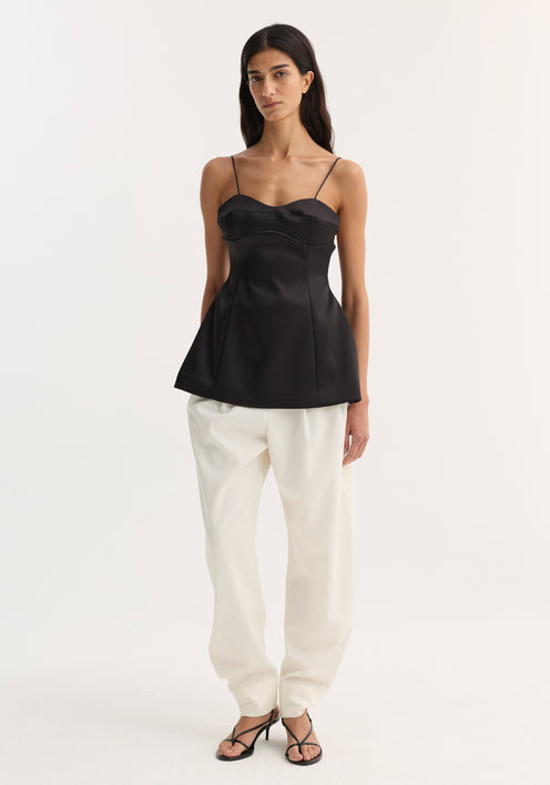 Bustier top | black with fitted waist, bustier-style stitching, and adjustable straps, worn by a model in loose white trousers and strappy sandals.