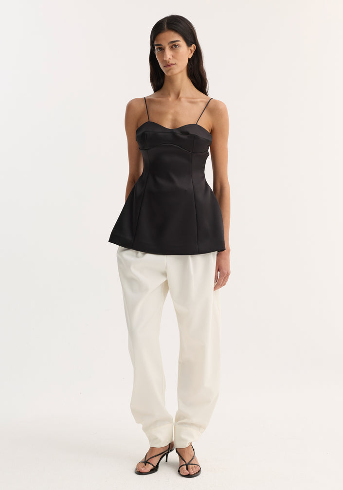 Bustier top | black with fitted waist, bustier-style stitching, and adjustable straps, worn by a model in loose white trousers and strappy sandals.