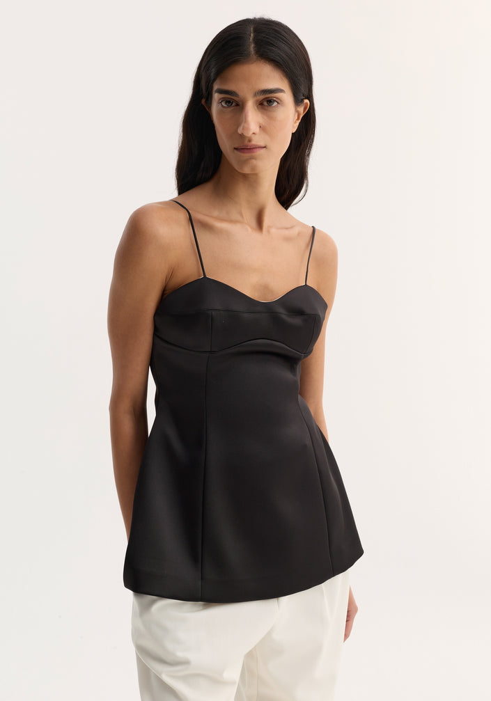 Bustier top | black with fitted waist, bustier-style stitching, and adjustable straps, worn by a model in loose white trousers and strappy sandals.