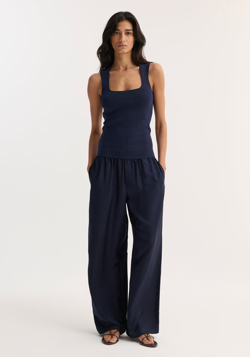 Woman in navy bustier-shaped knitted top with square neckline, paired with high-waisted wide-leg trousers and flat sandals, showcasing minimalist style.