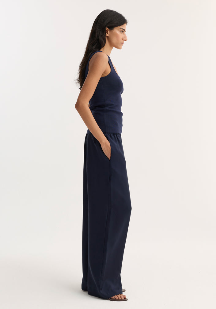 Woman in navy bustier-shaped knitted top with square neckline, paired with high-waisted wide-leg trousers and flat sandals, showcasing minimalist style.