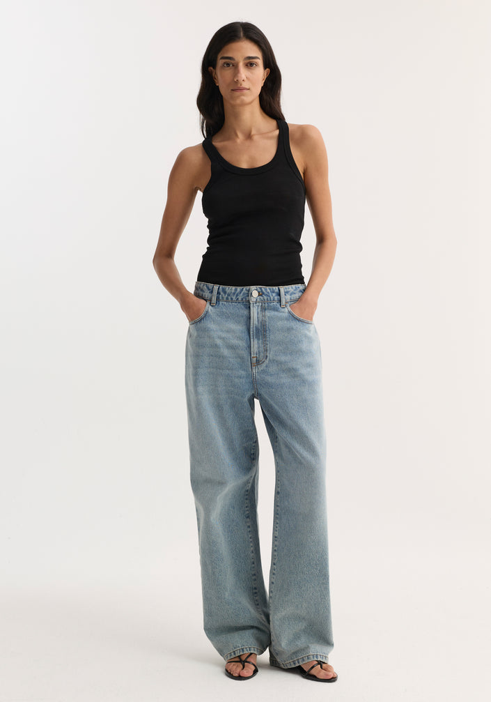 Merino scoop neck top in black worn by model; 100% wool, perfect for layering. Paired with wide-leg jeans and sandals. Model is 178cm, size 36.