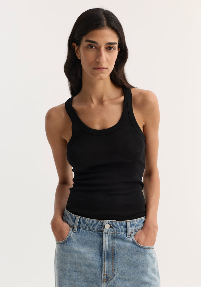 Merino scoop neck top in black worn by model; 100% wool, perfect for layering. Paired with wide-leg jeans and sandals. Model is 178cm, size 36.