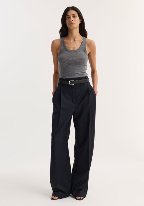 Person wearing a mid grey melange Merino scoop neck top with high-waisted black trousers, featuring pleats, a belt, and paired with black open-toed sandals.