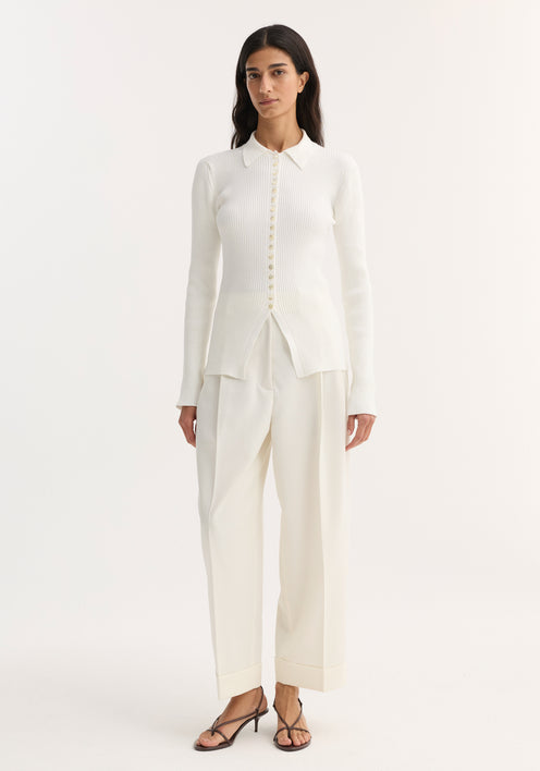 Model wearing the Elongated rib cardigan in off white, featuring a pointed collar, front buttons, and a hem slit, paired with wide-leg trousers and heels.