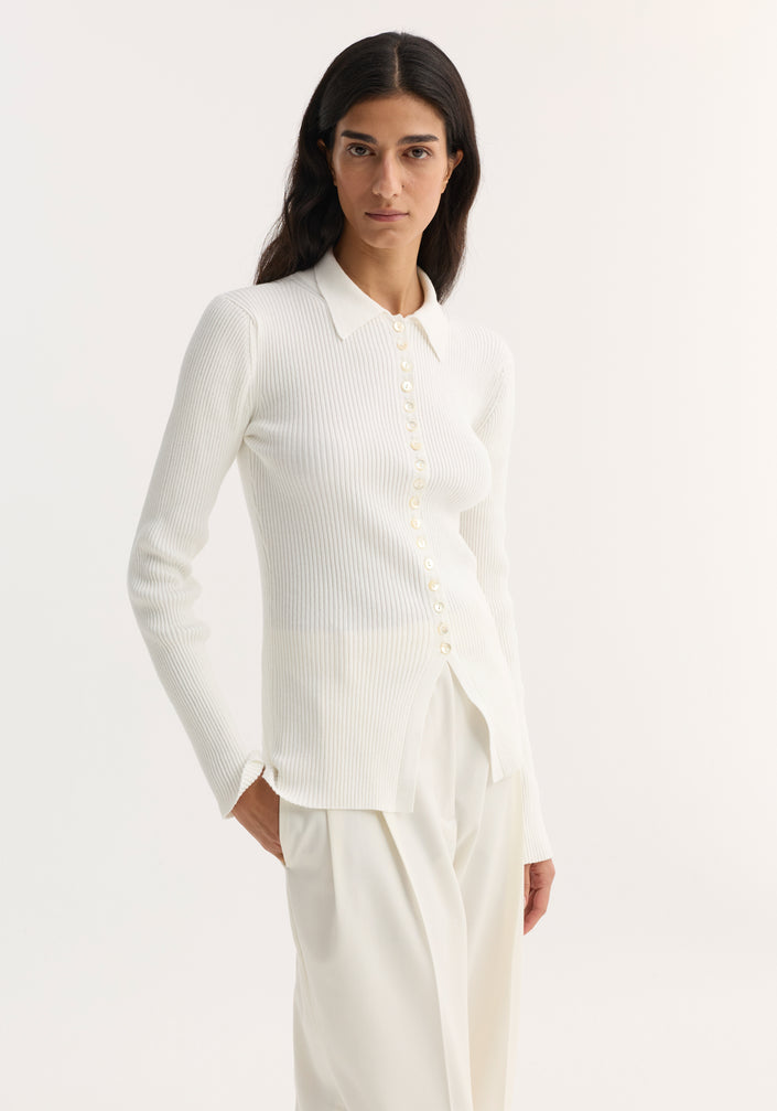 Model wearing the Elongated rib cardigan in off white, featuring a pointed collar, front buttons, and a hem slit, paired with wide-leg trousers and heels.