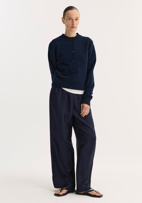 Model wearing a Short boiled cardigan in navy with a high crew neck, drop shoulders, and long sleeves, paired with wide-leg trousers and flip-flops.