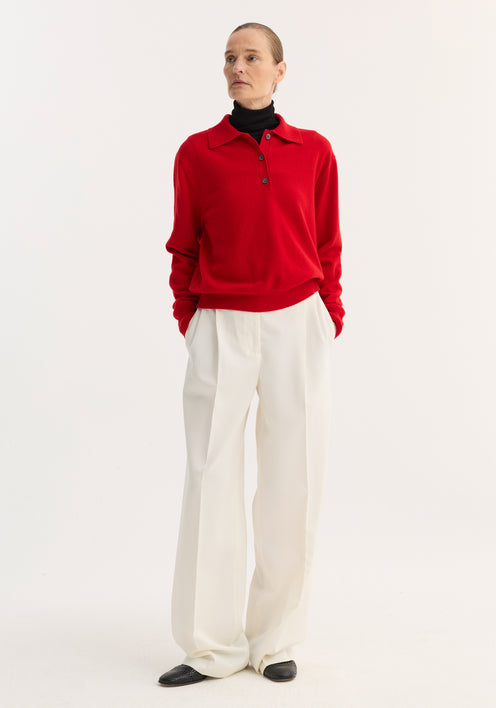 Model wearing a Wool Cashmere Polo | Red over a black turtleneck, paired with high-waisted white trousers, showcasing the polo's structured collar and three-button front.