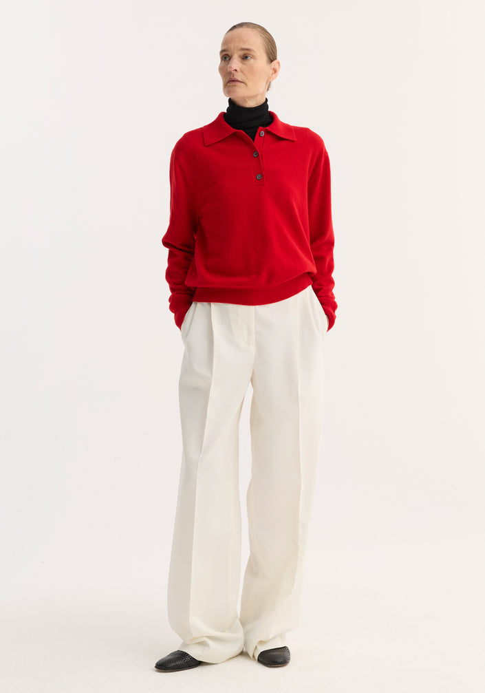 Model wearing a Wool Cashmere Polo | Red over a black turtleneck, paired with high-waisted white trousers, showcasing the polo's structured collar and three-button front.