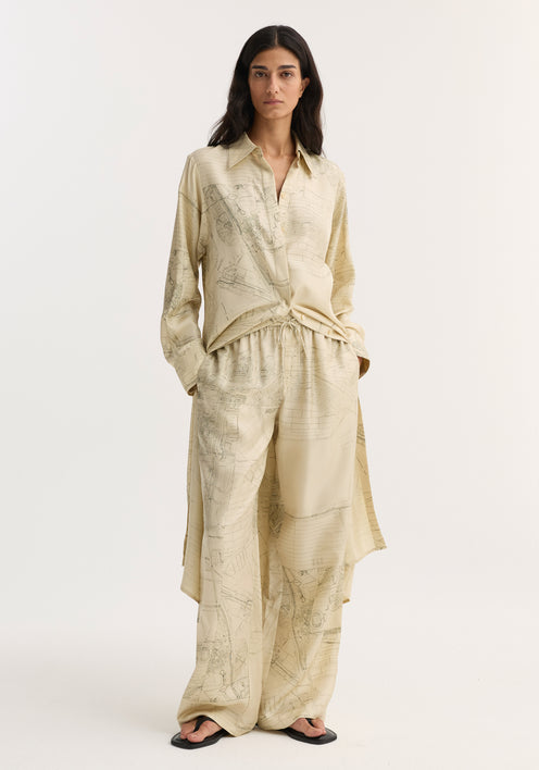 Woman in Wide leg silk trousers | Amsterdam, featuring archival map print, relaxed drape, elasticated waistband with drawstring, paired with matching button-down shirt and black sandals.