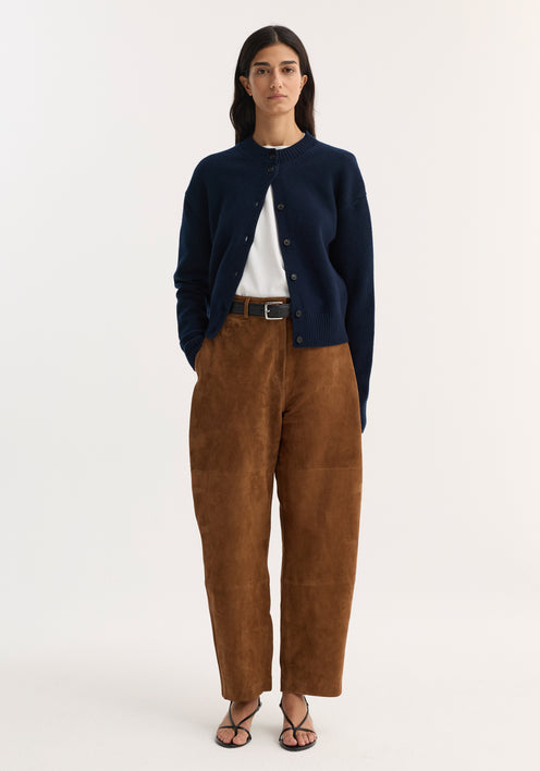 Woman wearing Suede barrel leg trouser | tobacco with brown suede, high-waisted, straight-leg design, button-front navy cardigan, black belt, and strappy sandals.