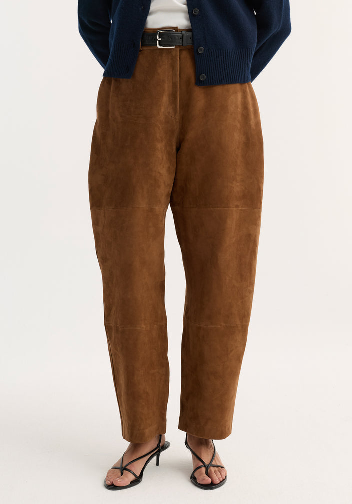 Woman wearing Suede barrel leg trouser | tobacco with brown suede, high-waisted, straight-leg design, button-front navy cardigan, black belt, and strappy sandals.