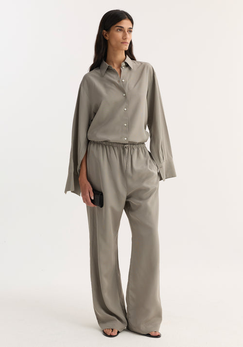 Woman wearing Relaxed fit trousers | light grey stripe, wide-leg with drawstring waist, paired with a matching shirt, black clutch, and sandals.