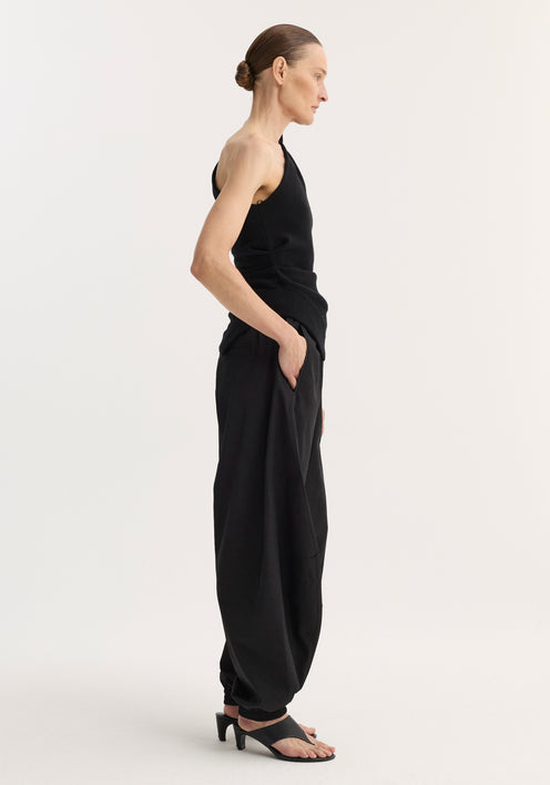 Person wearing black Balloon track pants with crinkled texture, elastic waistband, and cuffs, styled with a one-shoulder top and heeled sandals.