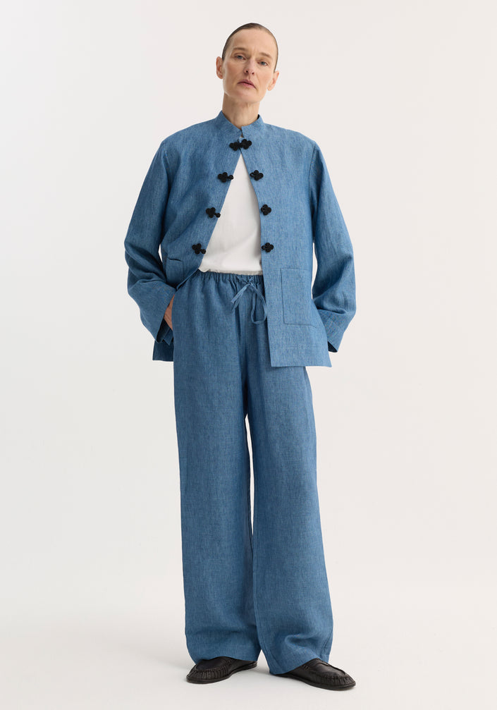 Model wearing Relaxed fit trousers in ocean blue, featuring a wide-leg design and drawstring waist, paired with a matching collarless jacket and black slip-on shoes.