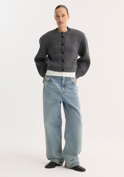 Model in Baggy fit denim | classic blue, showcasing low-waist, wide-leg jeans with a white tee, charcoal cardigan, and black slip-on shoes.