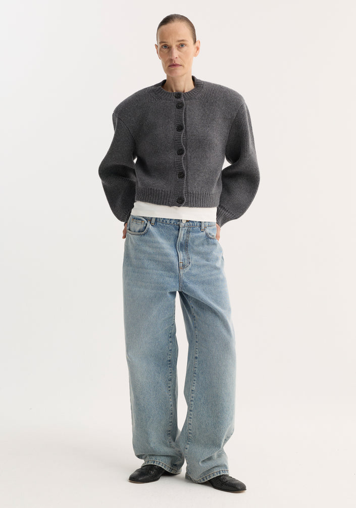 Model in Baggy fit denim | classic blue, showcasing low-waist, wide-leg jeans with a white tee, charcoal cardigan, and black slip-on shoes.