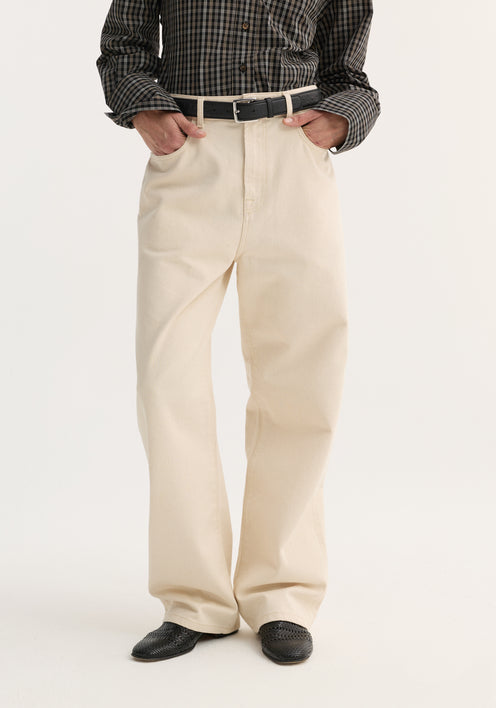 Person in dark plaid shirt with hands in pockets, showcasing Baggy fit denim | ecru with a relaxed, wide-leg, low-waist design and black slip-on shoes.