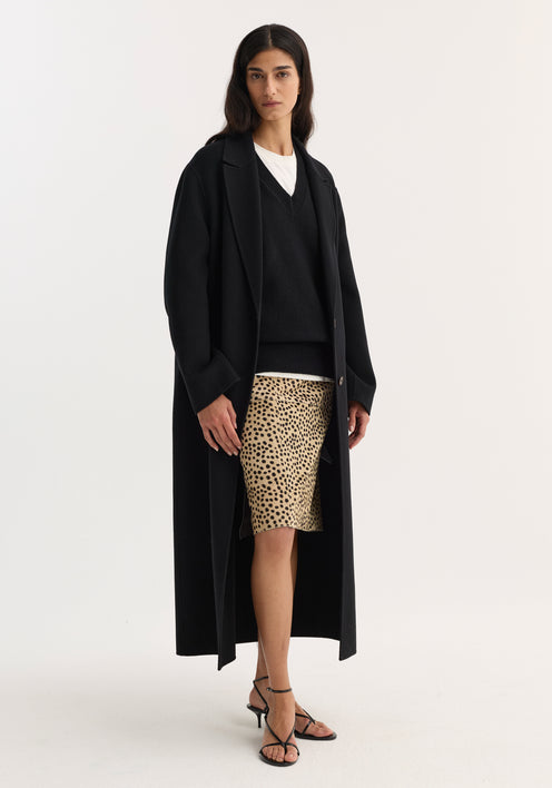 Model wearing a Pony hair pencil skirt in cheetah print, styled with a black overcoat, V-neck sweater, and strappy sandals against a plain background.