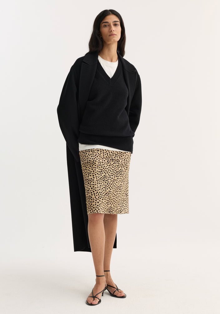 Model wearing a Pony hair pencil skirt in cheetah print, styled with a black overcoat, V-neck sweater, and strappy sandals against a plain background.