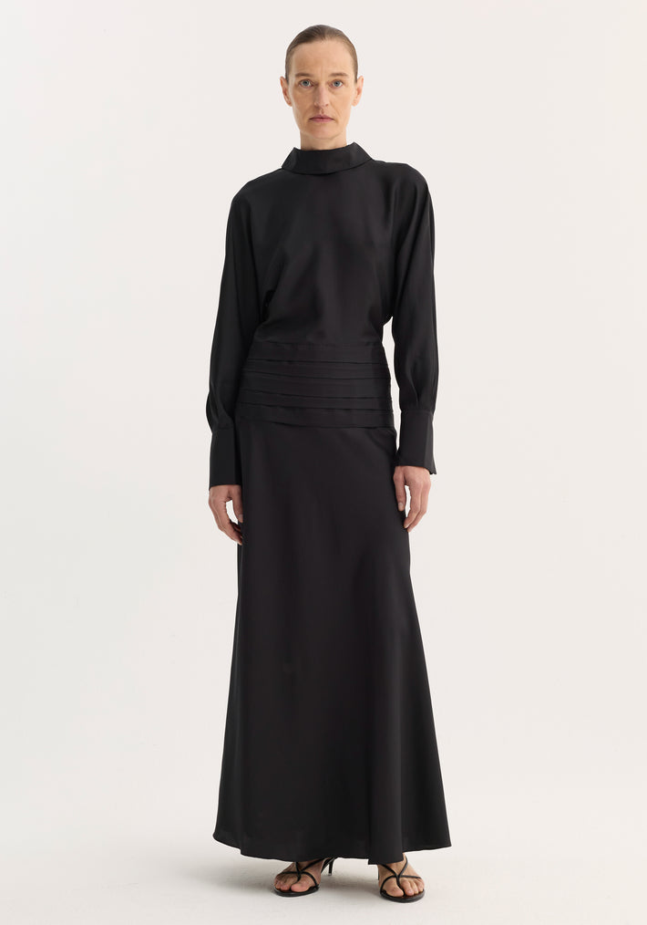 Tuxedo silk dress with high collar, pleated waist, open back, and long sleeves, worn by model standing with relaxed posture, showcasing elegant silhouette.