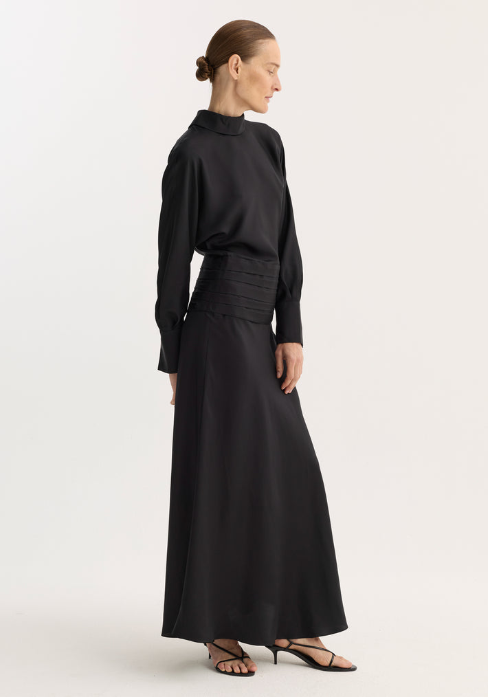 Tuxedo silk dress | black: Model in a long, flowing dress with high neckline, open back, cummerbund waist, and side zip, wearing strappy sandals.