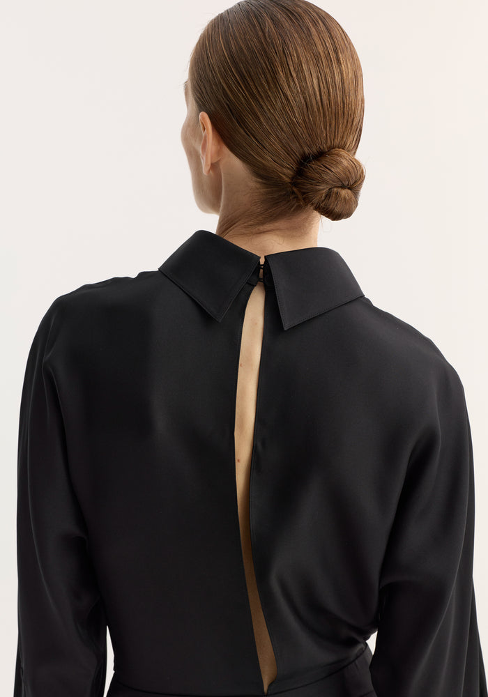 Back view of a model in a Tuxedo silk dress, showcasing the open back with cummerbund detailing and reversed collar. Hair styled in a low bun.