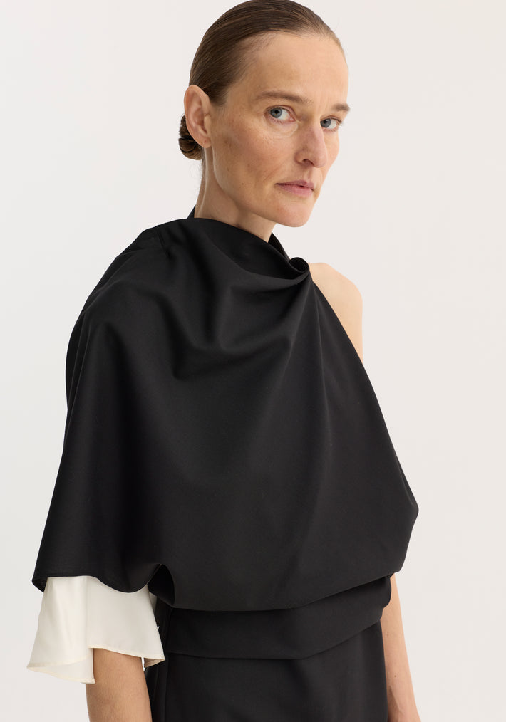 Woman wearing Draped open back dress | black, featuring sculptural one-shoulder design, single sleeve with silk insert, and back slit, highlighting elegant draping and silhouette.