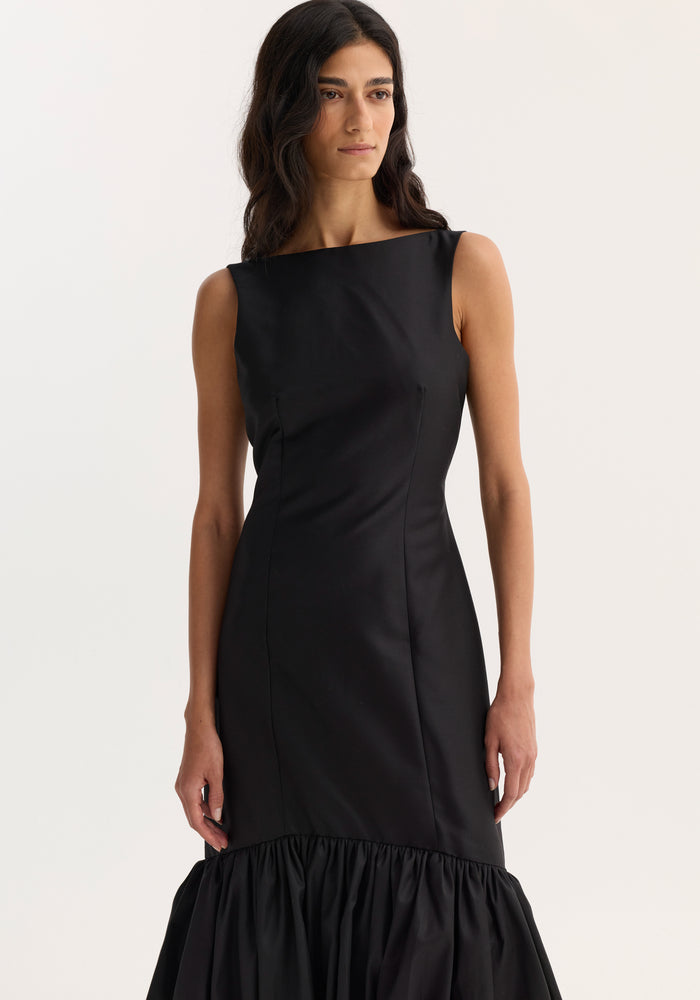 Voluminous dress | black: A model in a sleeveless, fitted dress with a boat neckline and peplum hem, showcasing tailored seam detailing for a refined fit.