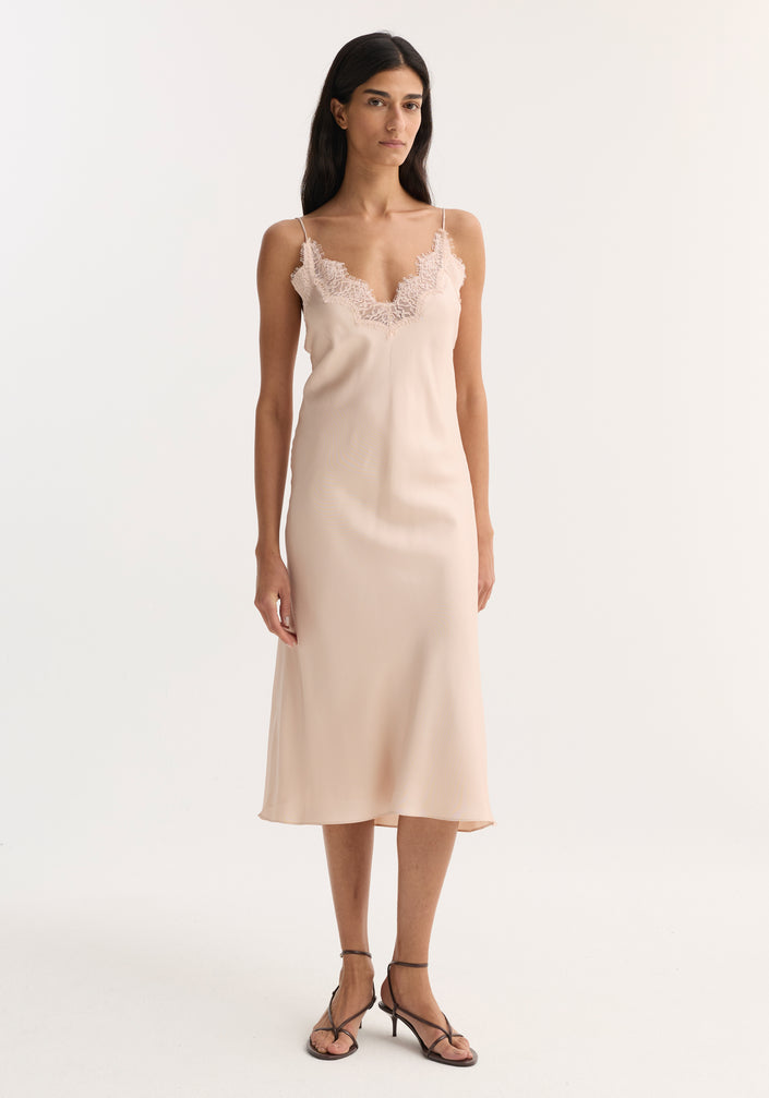 Model wearing Lace slip dress | rose, featuring a blush-pink silk slip dress with lace trim, V-neckline, spaghetti straps, and black strappy sandals.