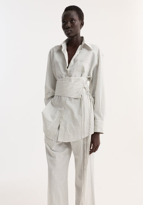 Model wearing a Silk Stripe Belted Shirt with wide sleeves and a wrap belt, paired with matching pin-stripe trousers and black flat sandals.