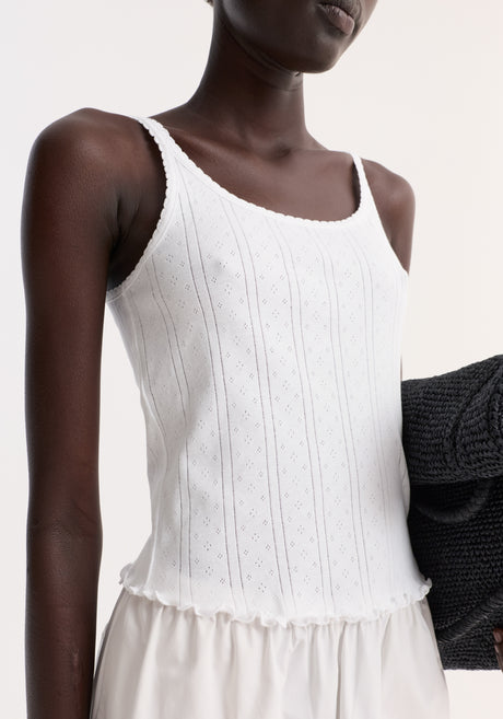 Model wearing Pointelle tank in off white, featuring a ribbed, sleeveless design with lettuce hem, paired with high-waisted trousers and holding a dark gray knit sweater.