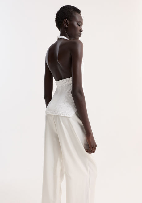 Model wearing Chunky knit halter top in optic white, featuring side slits and button closure, paired with loose trousers and black slide sandals.