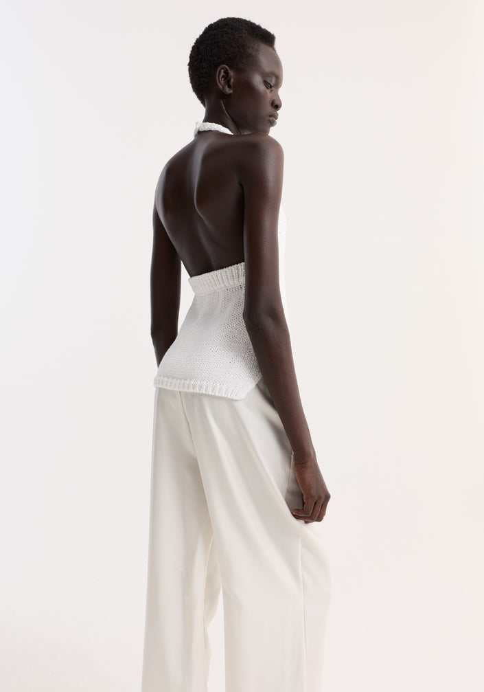 Model wearing Chunky knit halter top in optic white, featuring side slits and button closure, paired with loose trousers and black slide sandals.
