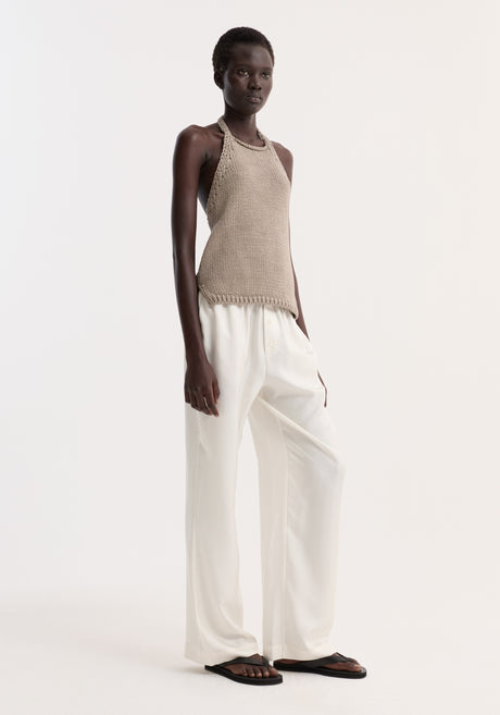Model wearing Chunky knit halter top | stone, featuring side slits and button neck closure, paired with wide-leg trousers and flip-flops in minimalist style.