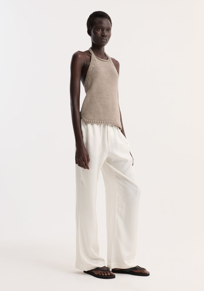 Model wearing Chunky knit halter top | stone, featuring side slits and button neck closure, paired with wide-leg trousers and flip-flops in minimalist style.