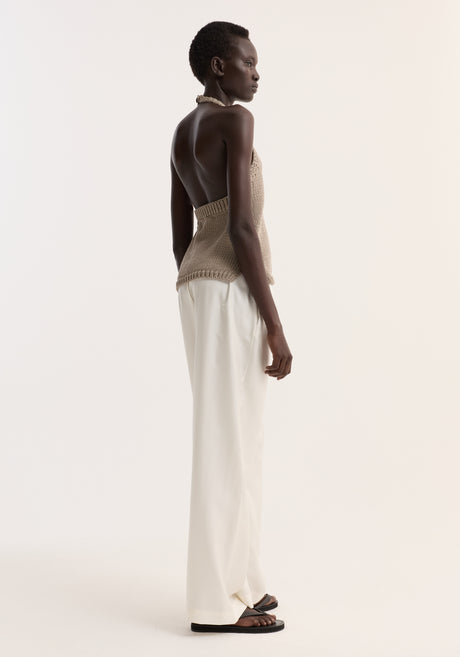 Model wearing Chunky knit halter top | stone, featuring side slits and button neck closure, paired with wide-leg trousers and flip-flops in minimalist style.
