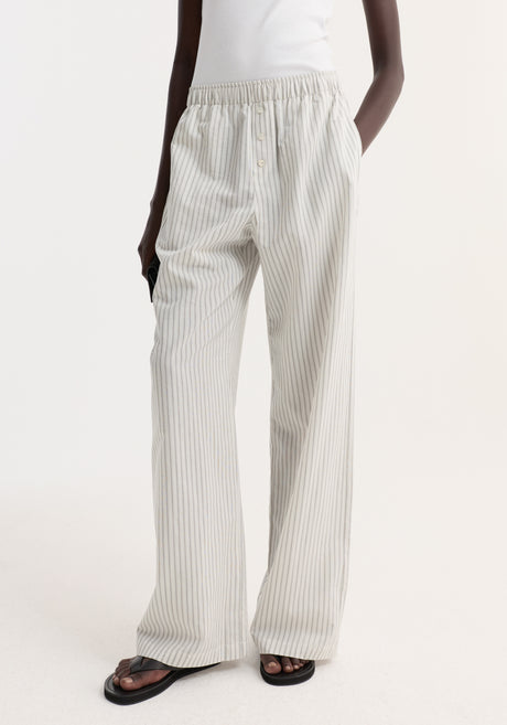 Model in Silk stripe pyjama trousers | fine stripe, featuring wide-leg design and elasticated waistband, paired with a white rib-tank and black sandals.